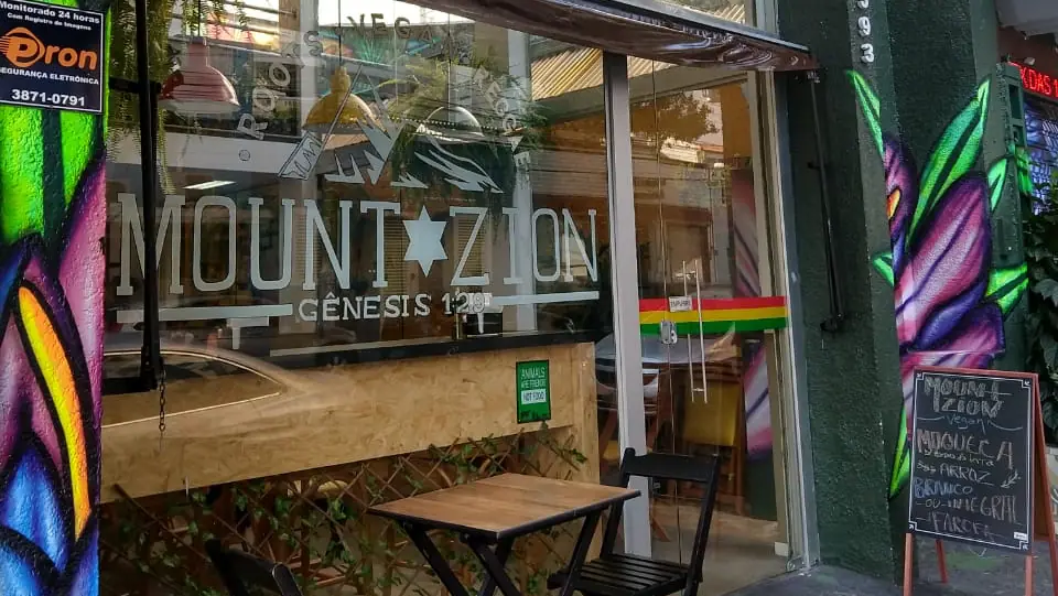Fachada do Mount Zion Vegan com letreiro e mesas na calçada