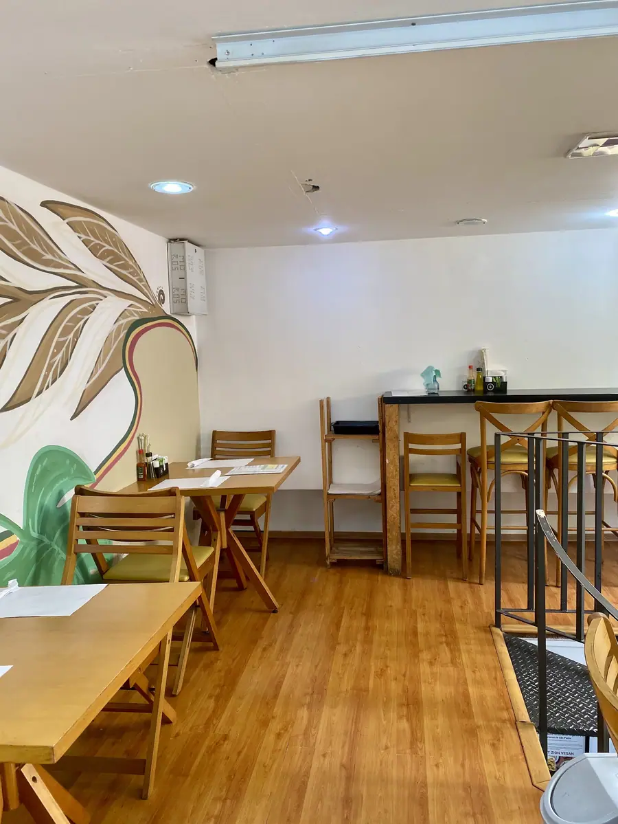 Salão do Mount Zion Vegan com mesas de madeira e parede com folhagens pintadas